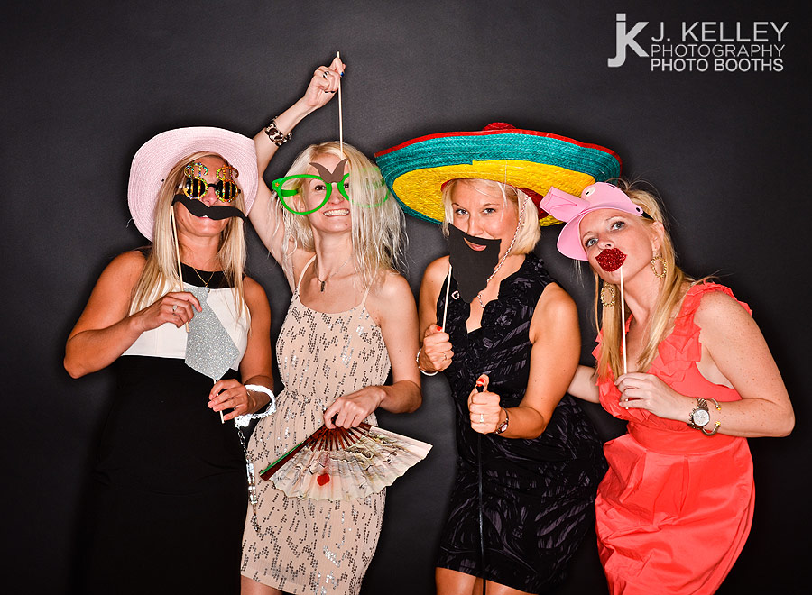 Wedding reception guests in Columbia, Missouri use props on a stick and hats to have fun taking their picture in a photo booth
